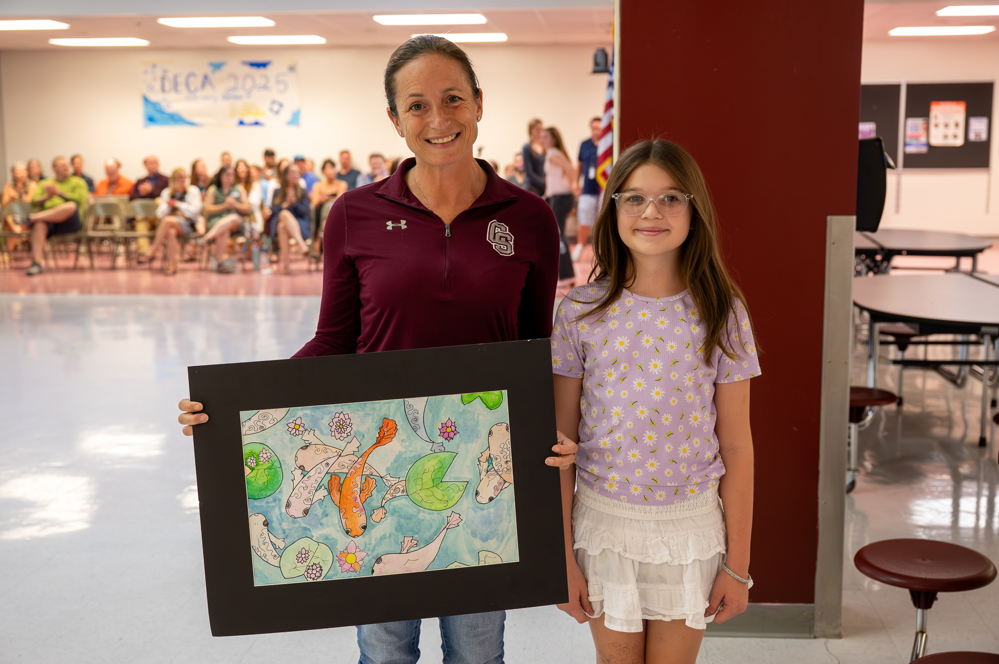 A board of education member standing proudly with a student, who gifted them artwork.